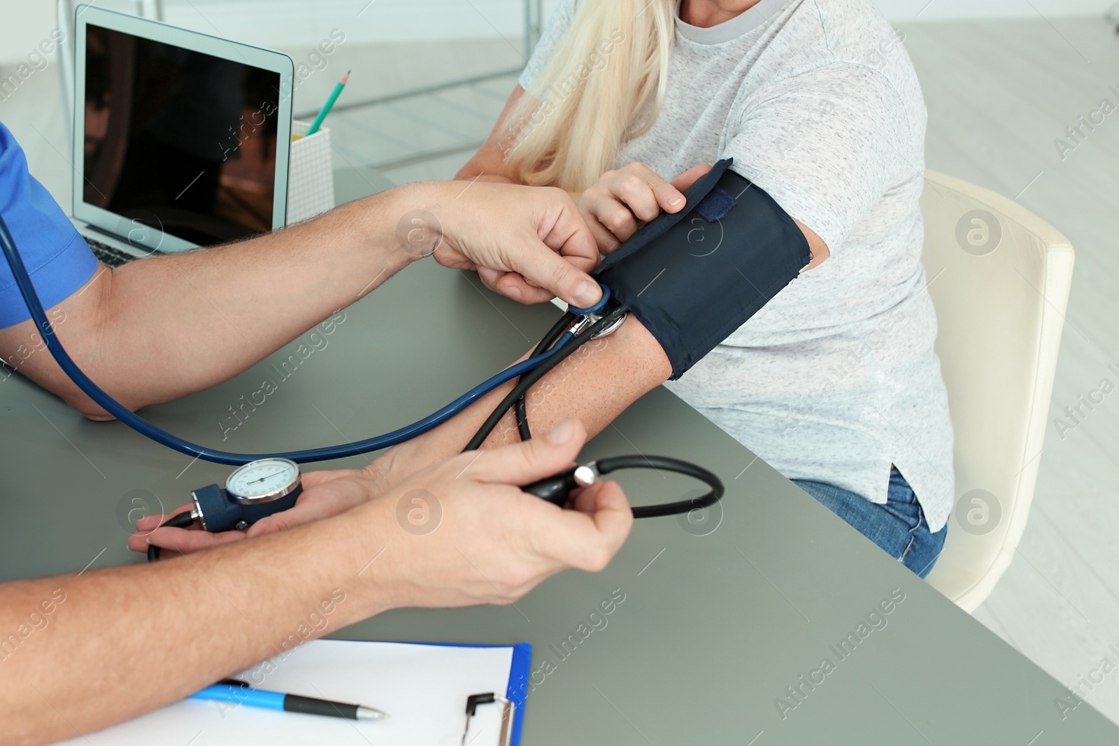Photo of Close up view of medical assistant measuring female patient blood pressure in clinic