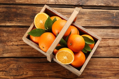 Photo of Delicious ripe oranges in basket on wooden table, top view