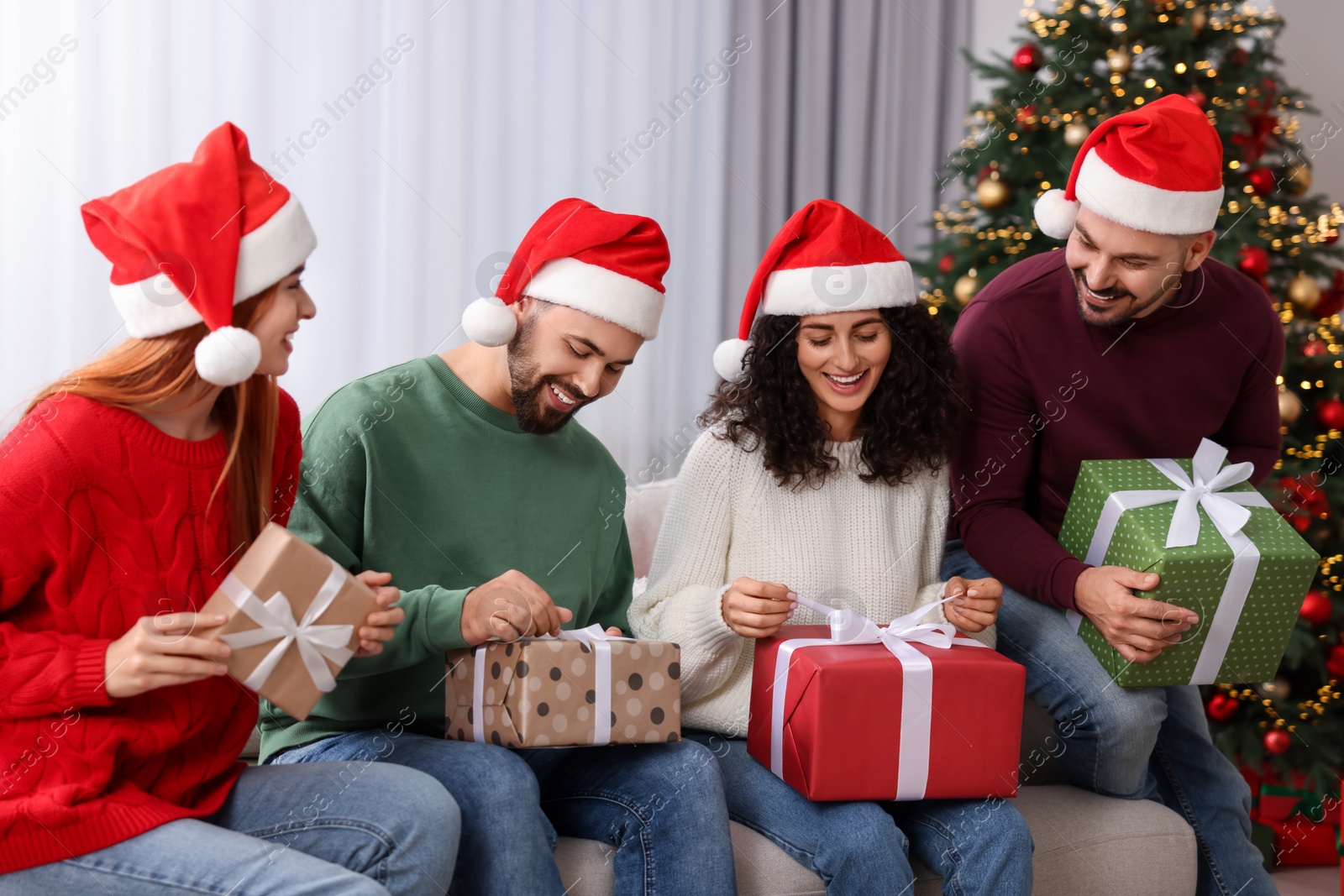 Photo of Christmas celebration in circle of friends. Happy woman and man opening gifts at home