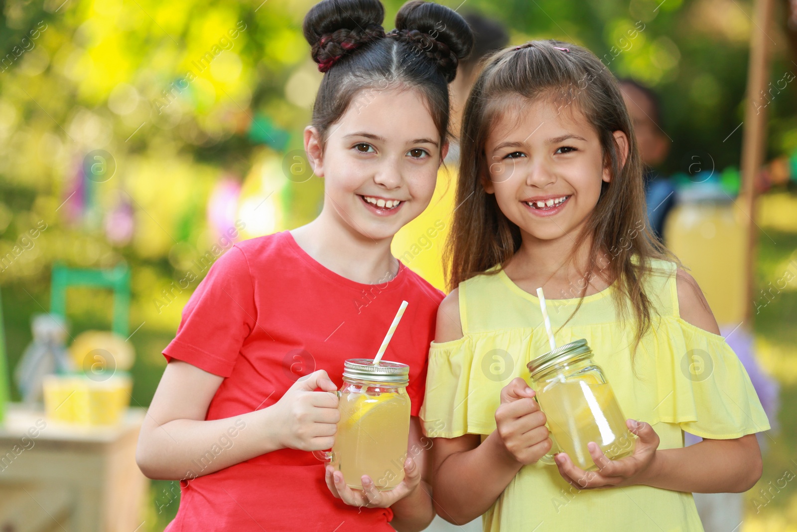 Photo of Cute little girls with natural lemonade in park. Summer refreshing drink