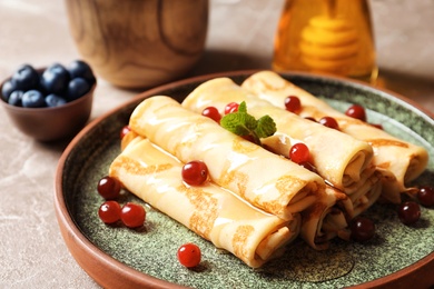 Photo of Thin pancakes with berries and honey on plate, closeup