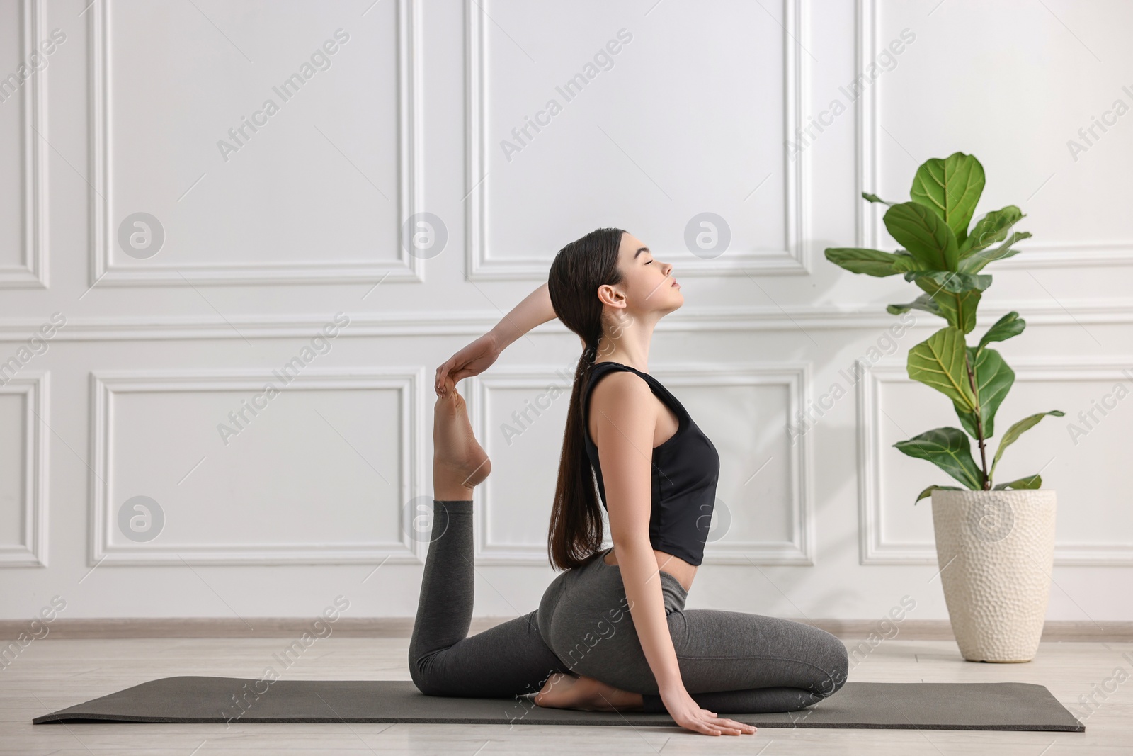 Photo of GIrl practicing one legged king pigeon asana on mat in yoga studio. Eka pada rajakapotasana pose