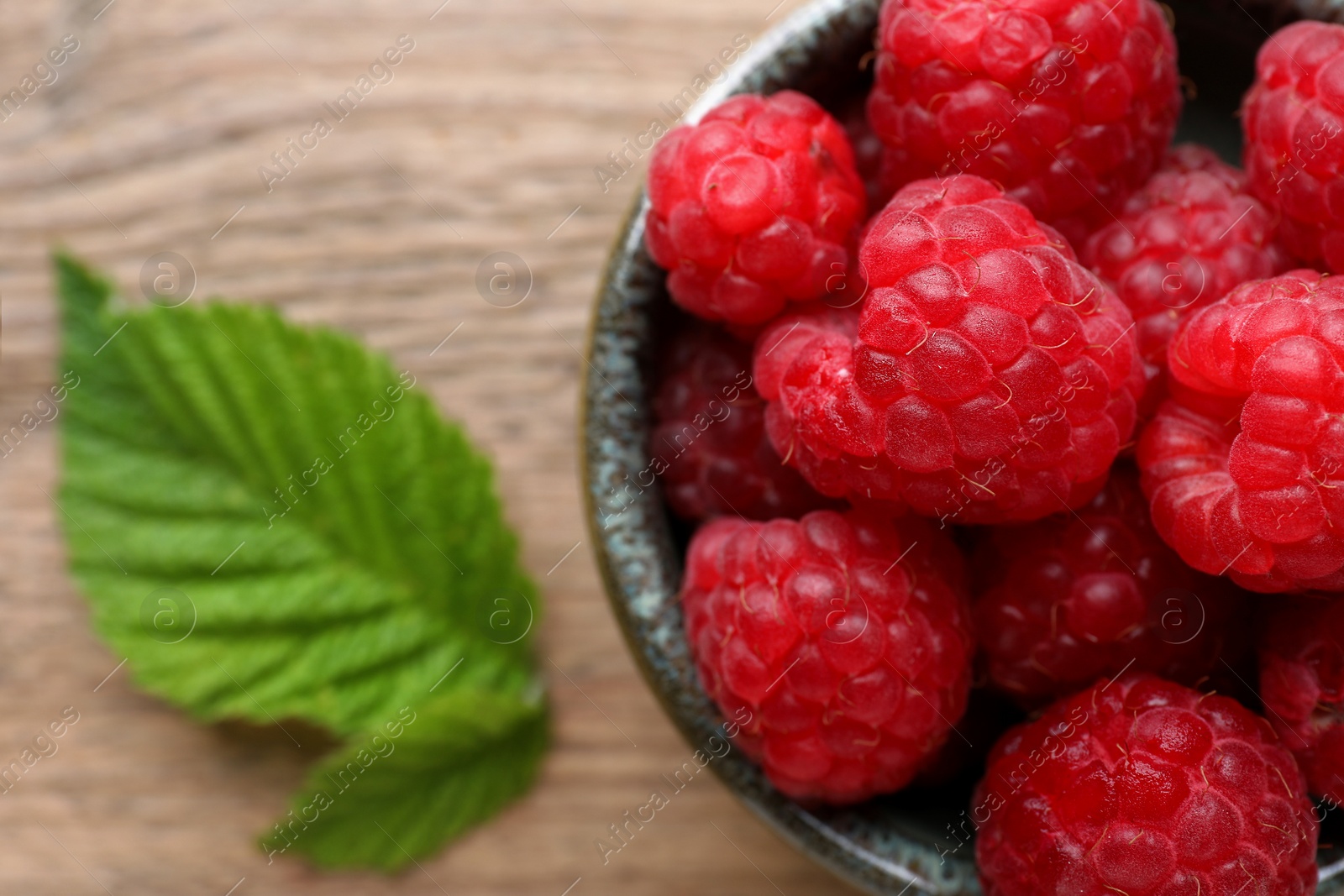 Photo of Tasty ripe raspberries and green leaves on wooden table, top view. Space for text