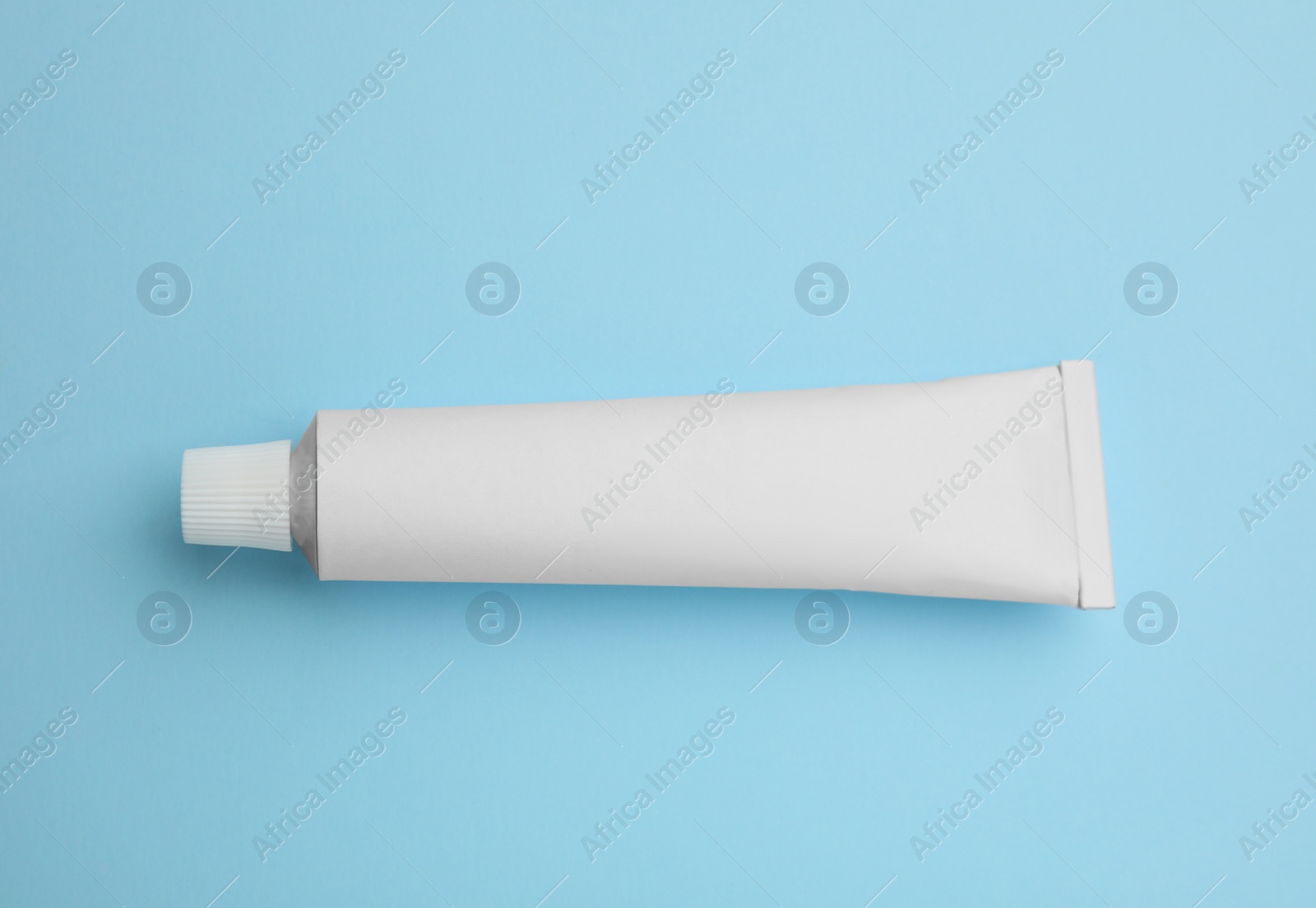 Photo of Blank white tube of ointment on light blue background, top view. Space for text