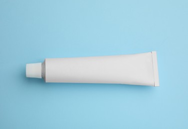 Photo of Blank white tube of ointment on light blue background, top view. Space for text