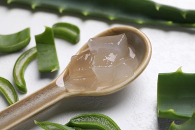 Photo of Aloe vera gel in spoon and slices of plant on white textured background, closeup
