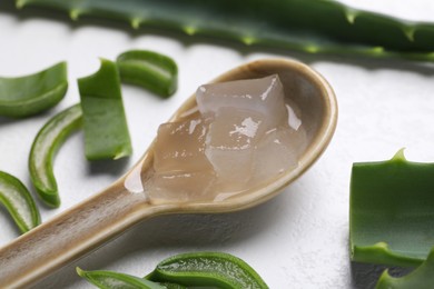 Aloe vera gel in spoon and slices of plant on white textured background, closeup