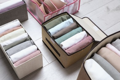 Photo of Different cases and organizer with folded clothes on white wooden background. Vertical storage