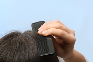 Photo of Woman with comb and dandruff in her dark hair on color background, closeup