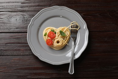 Photo of Heart made of tasty spaghetti, fork, tomato and basil on wooden table, top view