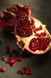 Photo of Pieces of ripe juicy red pomegranate with grains on grey textured table, closeup