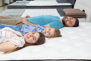 Photo of Happy family lying on new orthopedic mattress in store