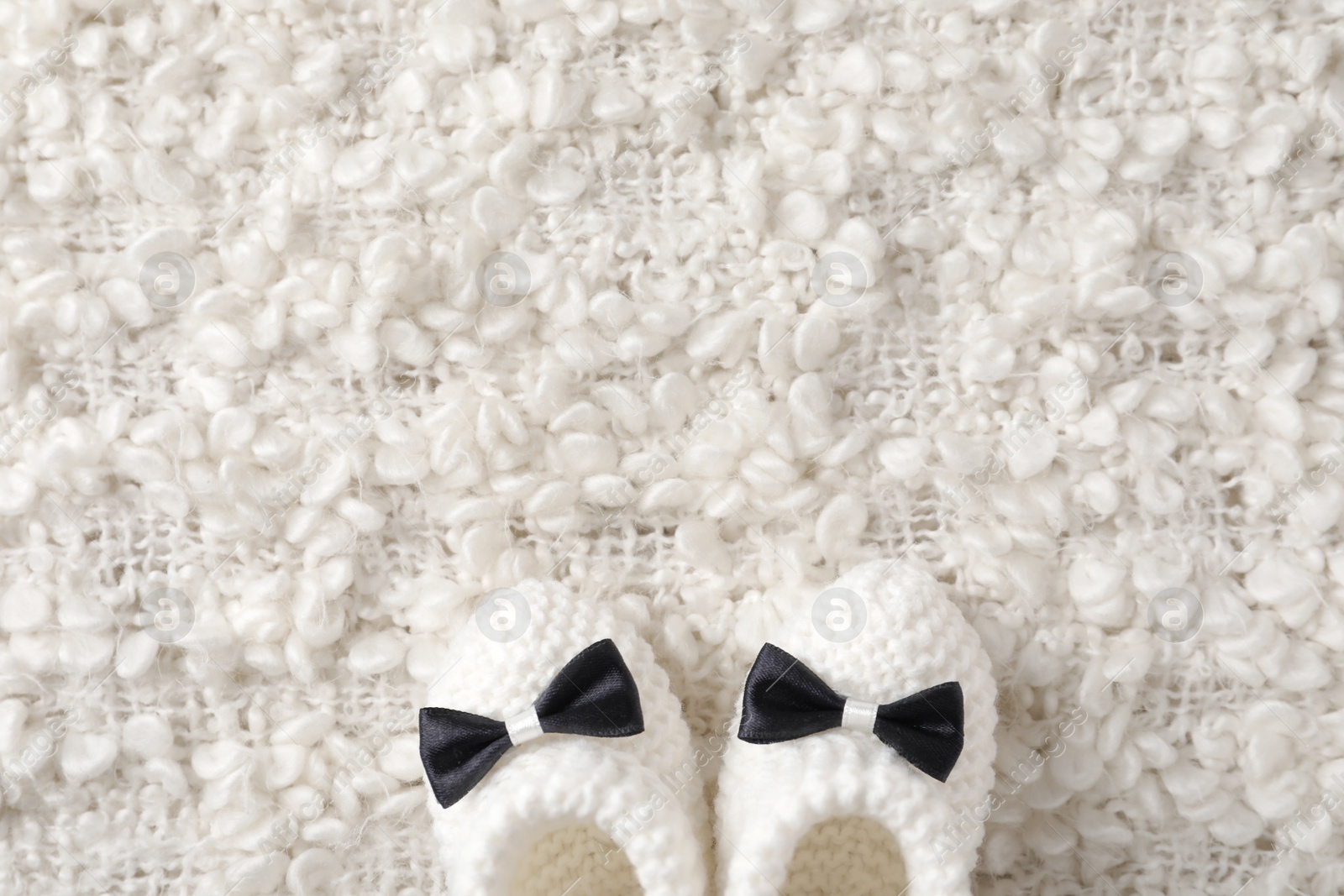 Photo of Handmade baby booties on soft plaid, top view with space for text