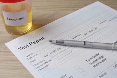 Photo of Drug test result form, container with urine sample and pen on wooden table, closeup