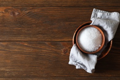 Photo of Organic salt in bowl on wooden table, top view. Space for text