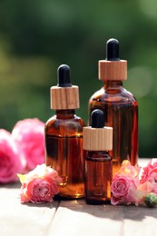 Bottles of rose essential oil and flowers on wooden table outdoors
