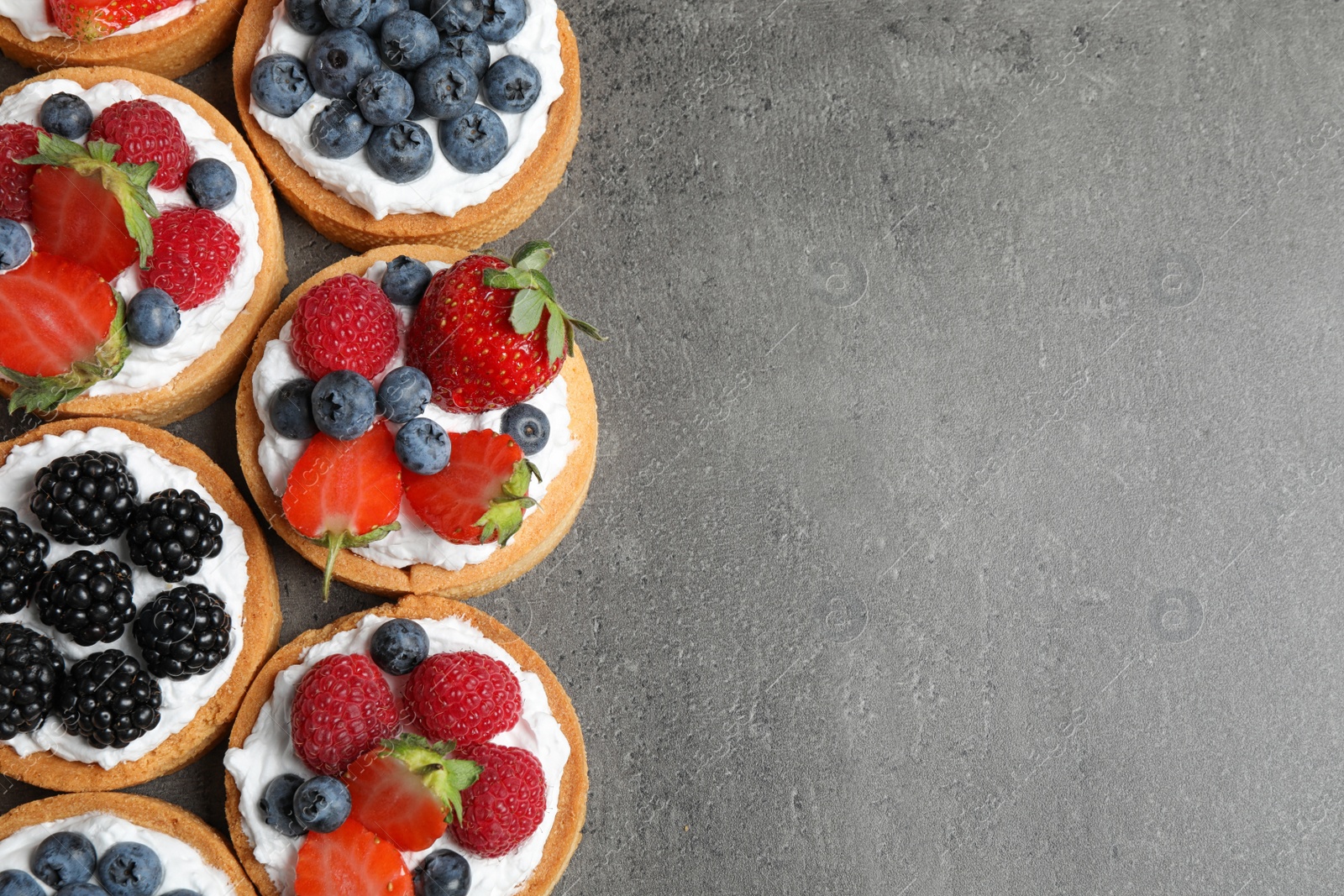 Photo of Tarts with different berries on grey table, top view with space for text. Delicious pastries