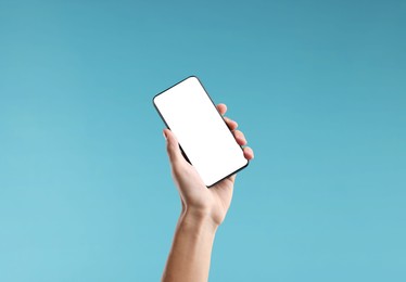 Photo of Man holding smartphone with blank screen on light blue background, closeup. Mockup for design