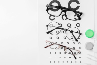 Vision test chart, glasses, lenses and tweezers on white background, flat lay. Space for text