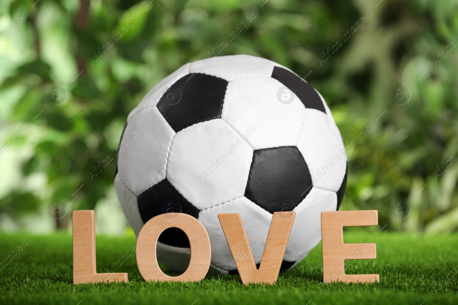 Photo of Football ball and word Love on green grass against blurred background