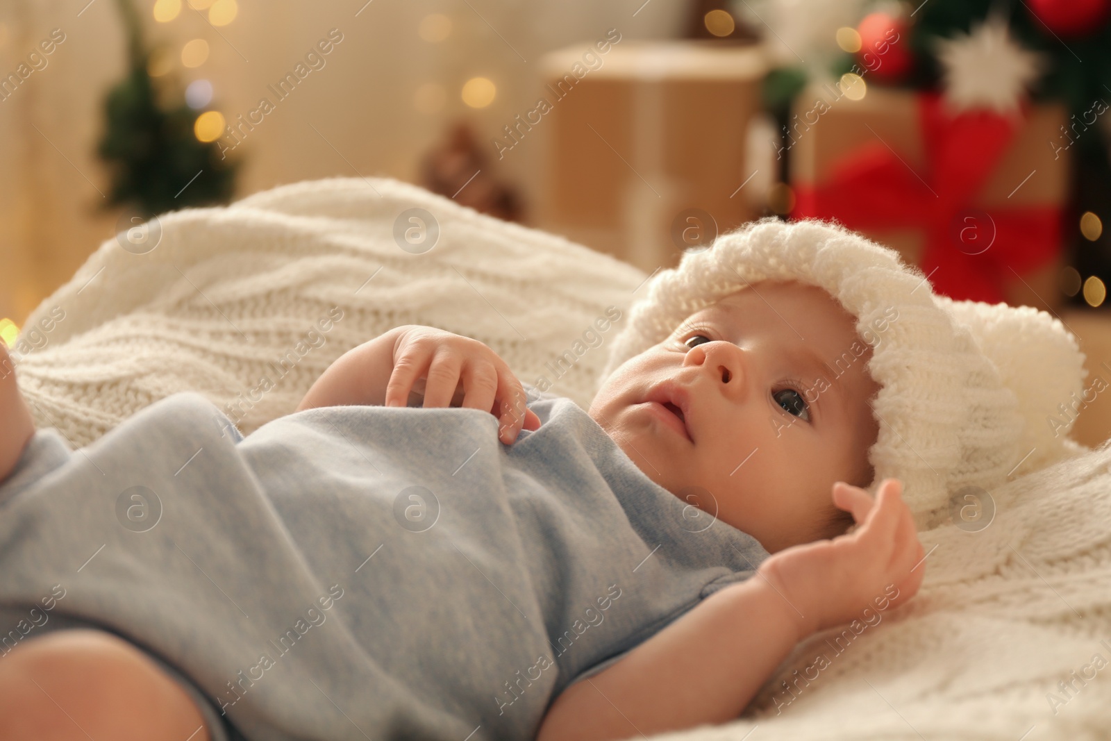 Photo of Cute little baby on knitted blanket in room decorated for Christmas