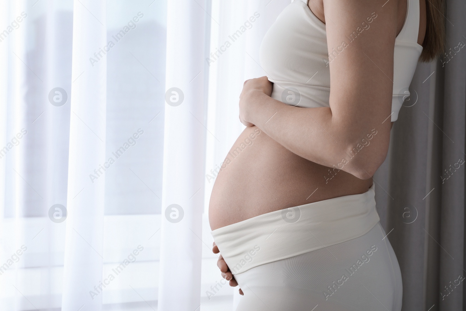 Photo of Pregnant woman near window at home, closeup. Space for text