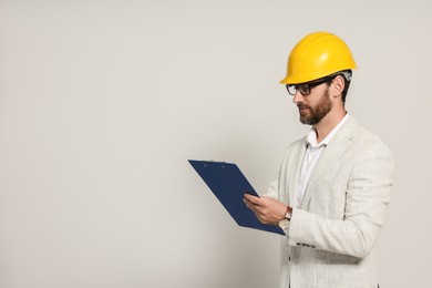 Photo of Professional engineer in hard hat with clipboard on white background, space for text