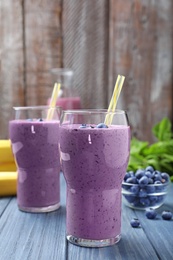 Photo of Glasses of delicious blueberry smoothie on blue wooden table