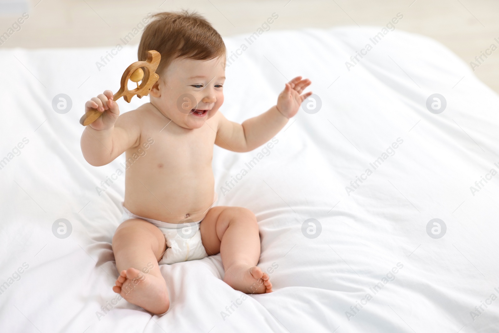 Photo of Happy baby boy with wooden rattle on bed at home. Space for text
