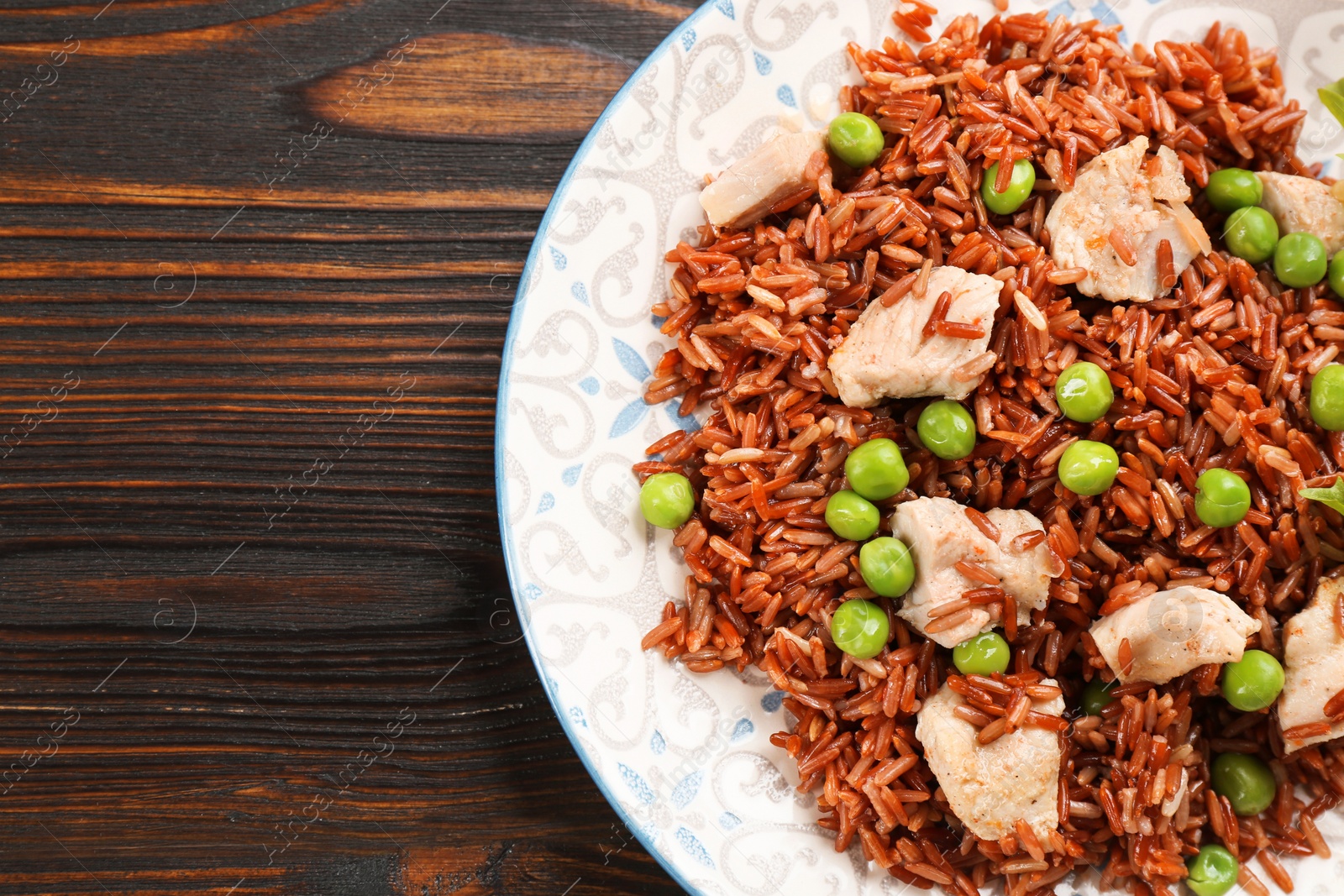 Photo of Tasty brown rice with meat and vegetables on wooden table, top view