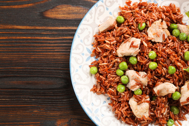 Photo of Tasty brown rice with meat and vegetables on wooden table, top view