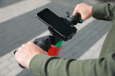 Photo of Man riding electric kick scooter with smartphone outdoors, closeup