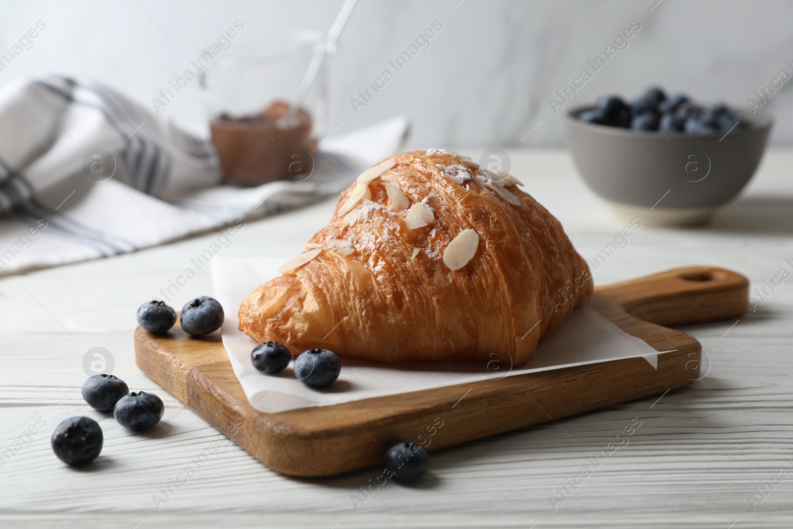Photo of Delicious croissant with almond flakes and blueberries on white wooden table, closeup