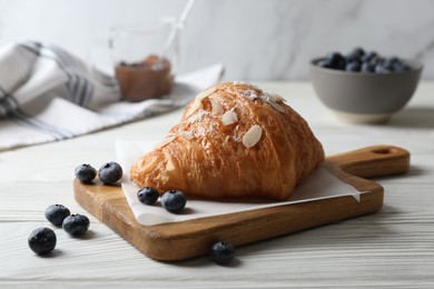 Delicious croissant with almond flakes and blueberries on white wooden table, closeup