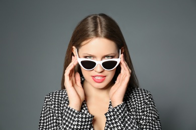 Young woman wearing stylish sunglasses on grey background