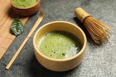 Photo of Cup of fresh green matcha tea, bamboo whisk and spoon on grey table