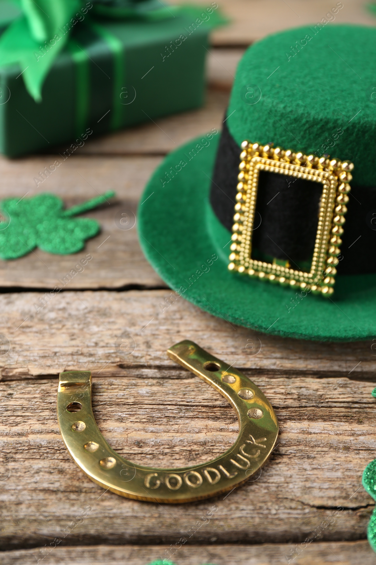 Photo of St. Patrick's day. Leprechaun hat, golden horseshoe, green gift box and decorative clover leaves on wooden background, closeup
