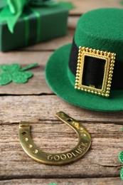 St. Patrick's day. Leprechaun hat, golden horseshoe, green gift box and decorative clover leaves on wooden background, closeup