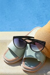 Photo of Stylish sunglasses, visor cap and slippers at poolside on sunny day. Beach accessories