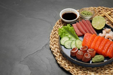 Photo of Tasty salmon slices, shrimp, cucumber and tuna on black table, space for text. Delicious sashimi set