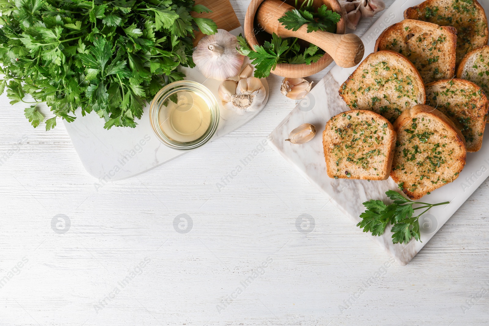 Photo of Slices of toasted bread with garlic and herbs served on white wooden table, flat lay. Space for text