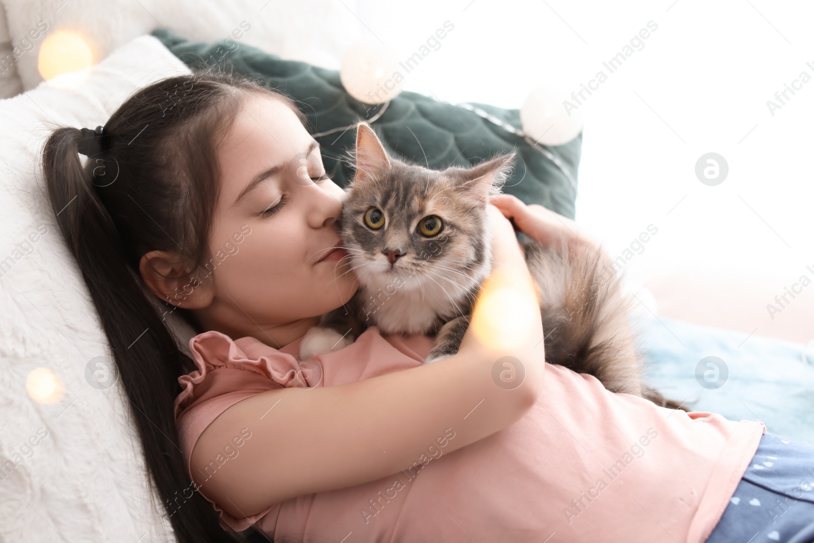 Photo of Cute little girl with cat lying on bed at home