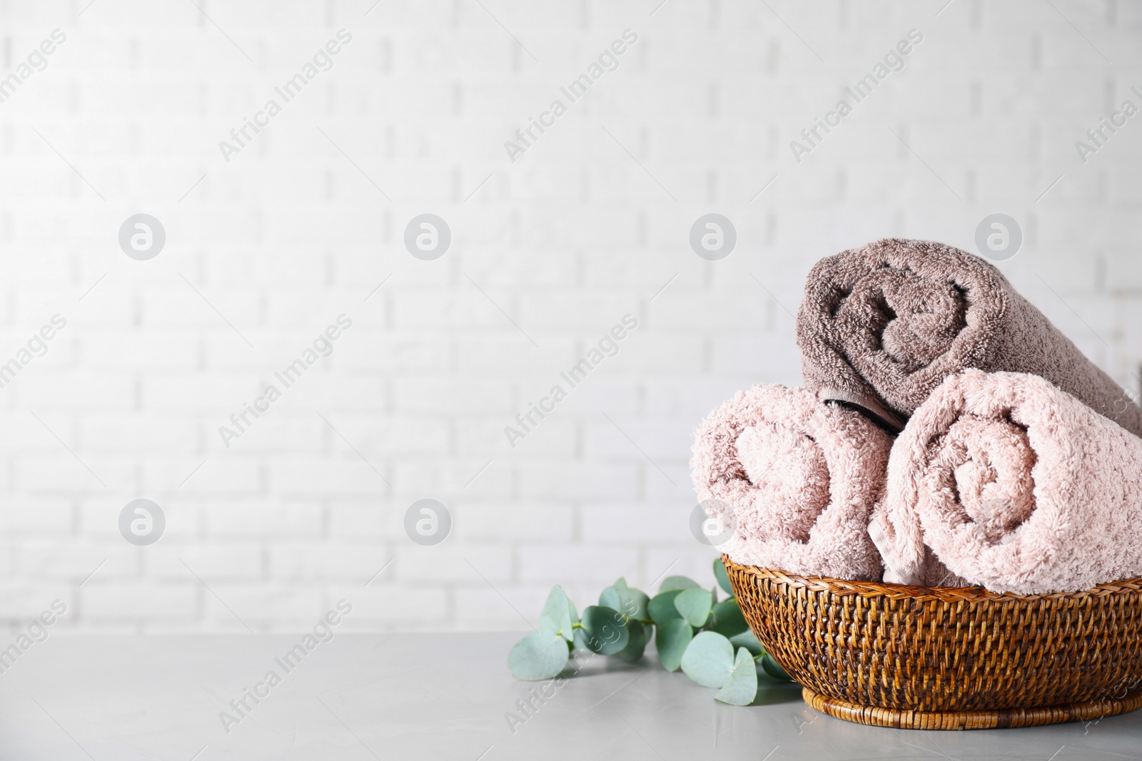 Photo of Wicker basket with rolled bath towels and eucalyptus branch near white brick wall. Space for text