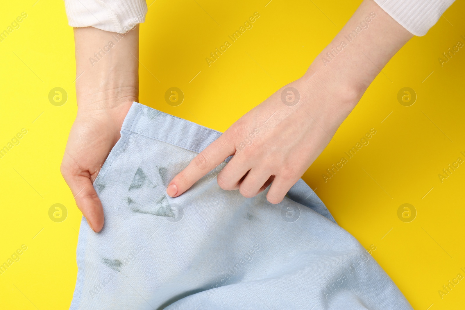 Photo of Woman showing shirt with stain on yellow background, top view