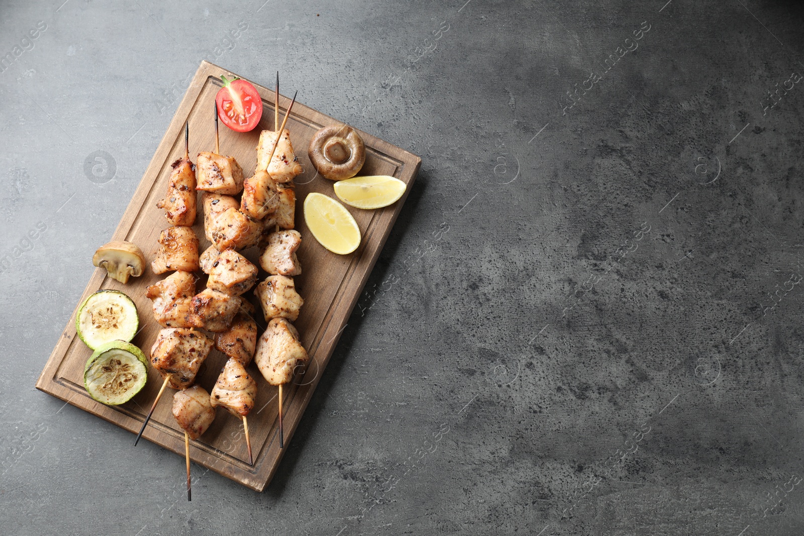 Photo of Delicious shish kebabs with vegetables and lemon on grey table, top view. Space for text