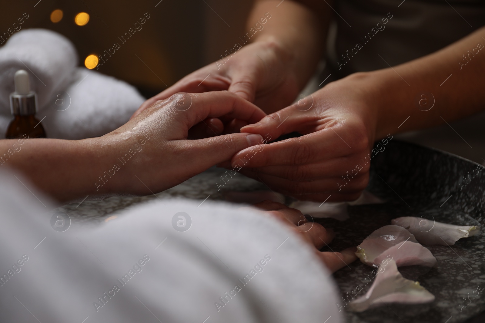 Photo of Woman receiving hand massage above bowl of water with flower petals in spa salon, closeup.