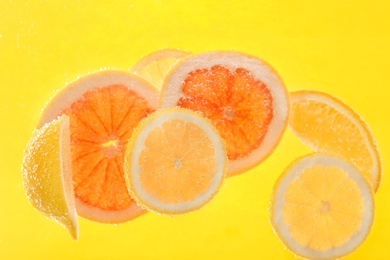 Slices of different citrus fruits in sparkling water on yellow background