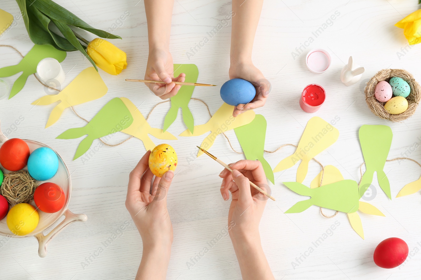 Photo of Mother and her child painting Easter eggs at table, top view