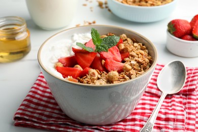 Bowl with tasty granola and strawberries served on white table, closeup. Healthy meal