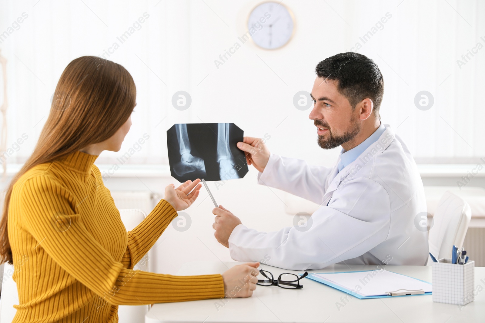 Photo of Orthopedist showing X-ray picture to patient at table in clinic